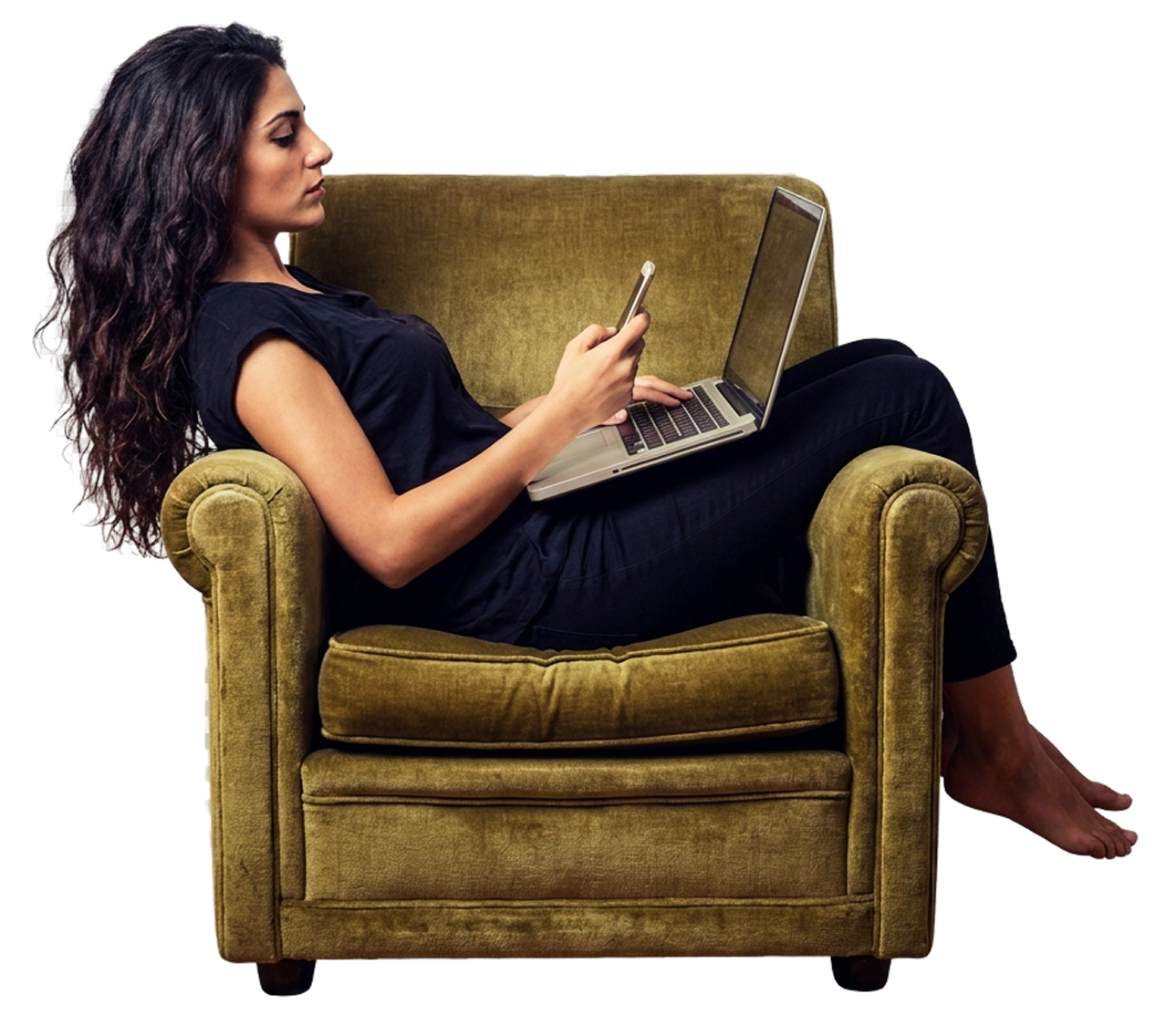 A woman relaxing sideways in a mustard velvet armchair, using a laptop and phone