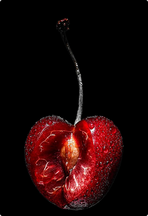 A split dark-red cherry with stem on black